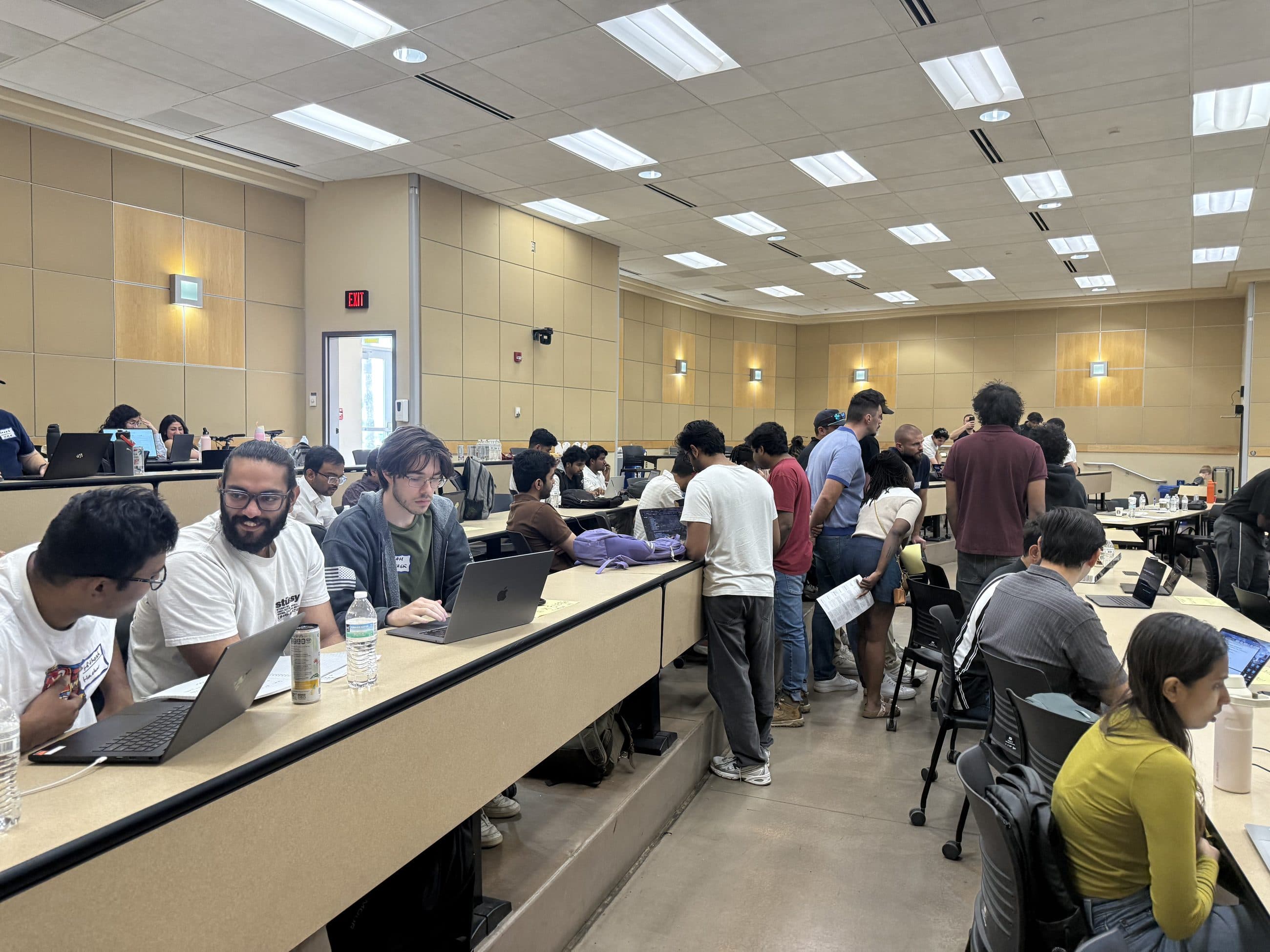 A full lecture hall of students working at laptops along tiered benches during the 2026 ASU Energy Hackathon, with others standing and talking in the aisle.